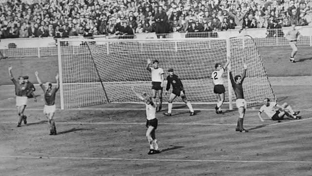 Die englischen Spieler – Roger H. (links), Bobby Charlton und der Torschütze Geoff Hurst (rechts) – wenden sich an den Schiedsrichter, während die westdeutschen Spieler protestieren, nachdem Hurst das umstrittene dritte Tor für England erzielt hatte. Die englischen Spieler – Roger H. (links), Bobby Charlton und der Torschütze Geoff Hurst (rechts) – wenden sich an den Schiedsrichter, während die westdeutschen Spieler protestieren, nachdem Hurst das umstrittene dritte Tor für England erzielt hatte.