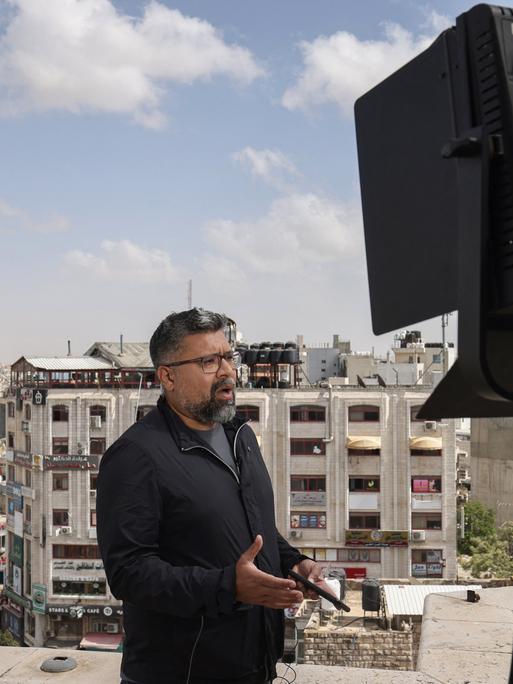 Ein Korrespondent steht während einer Live-Sendung auf einem Dach in Ramallah und spricht, im Hintergrund sind die Dächer der Stadt zu sehen.