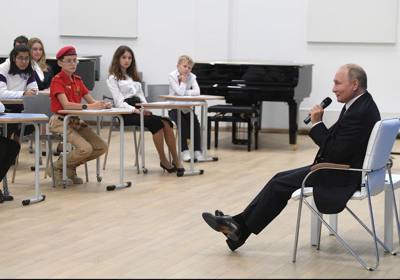 Wladimir Putin sitzt auf einem Stuhl vor einer Schulklasse und spricht durch ein Mikrofon zu ihnen.