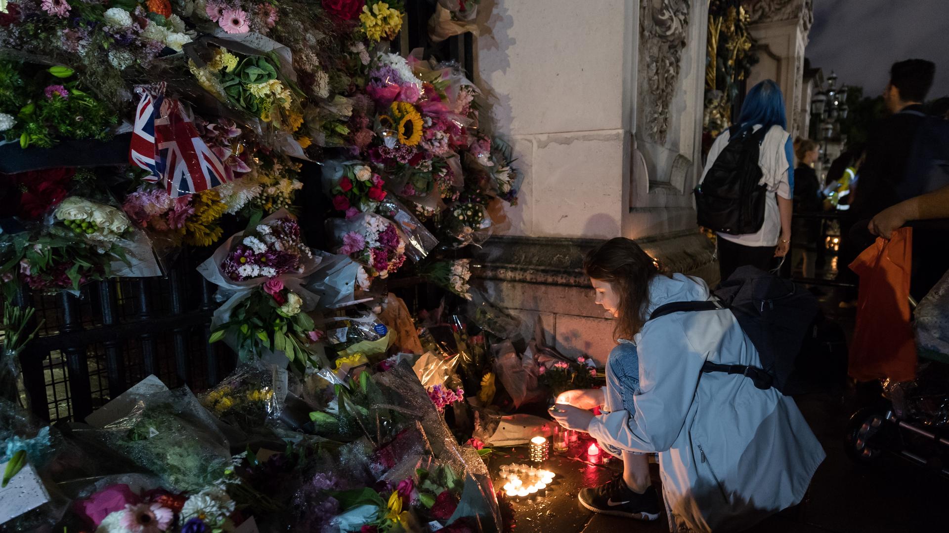Queen Elizabeth II. ist tot: Vor dem Buckingham Palace in London zündet eine Frau eine Kerze inmitten eines Blumenmeeres an