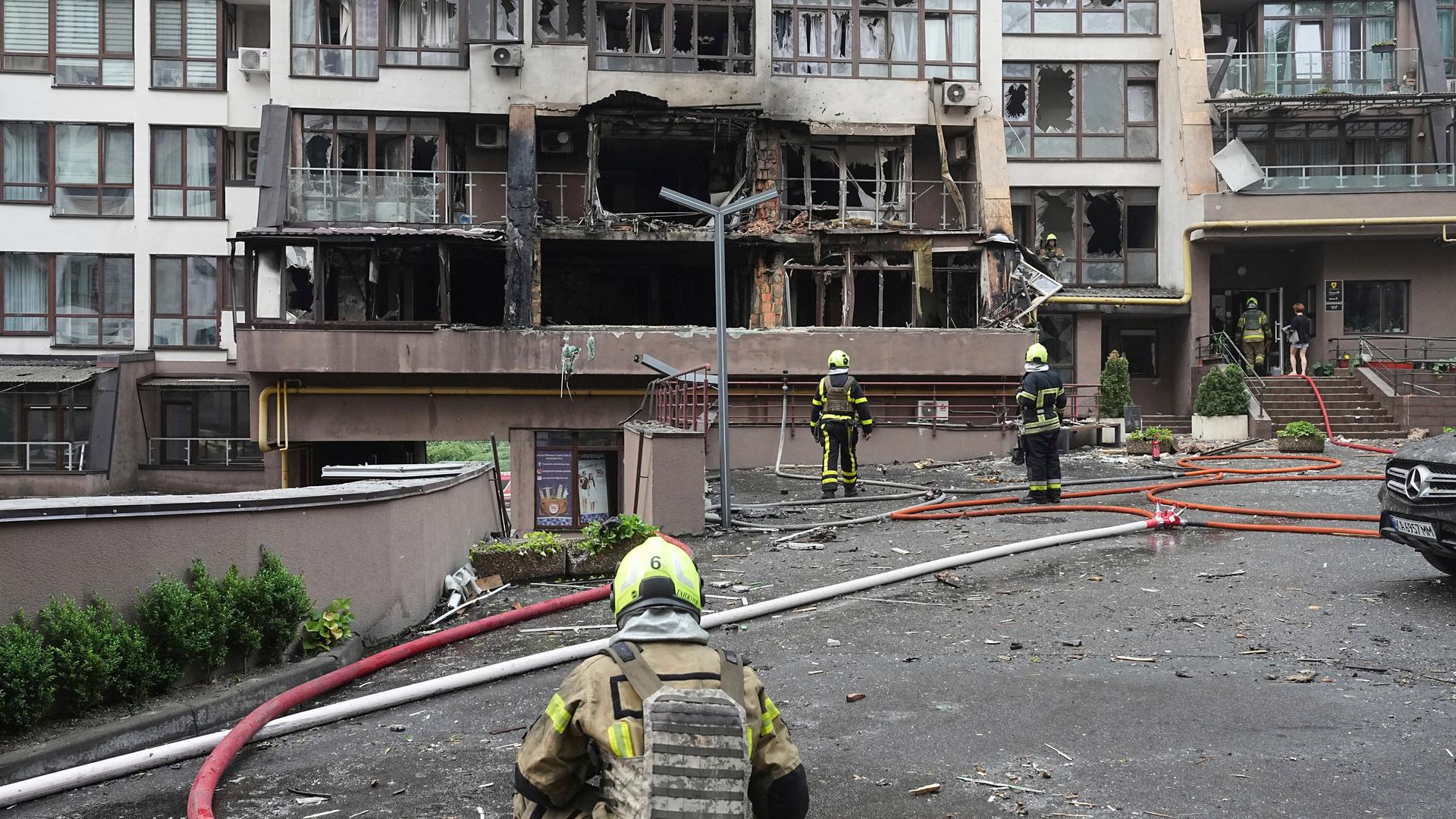 Feuerwehrleute arbeiten an und in einem zerstörten und verkohlten Wohnhaus. Davor liegen Feuerwehrschläuche.