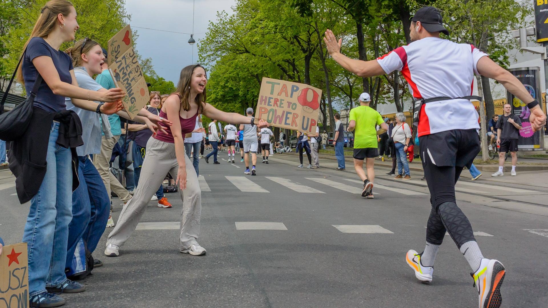 Zuschauer und Zuschauerinnen stehen in Wien am Straßenrand und bejubeln die Marthonläufer und -läuferinnen.