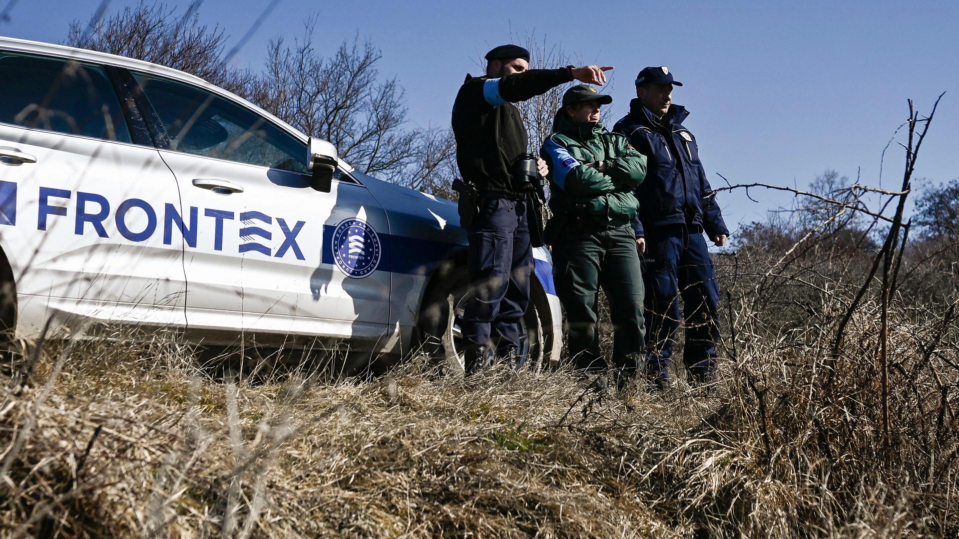 Drei uniformierte Männer stehen neben einem Wagen mit dem Frontex-Schriftzug und beobachten die Umgebung.