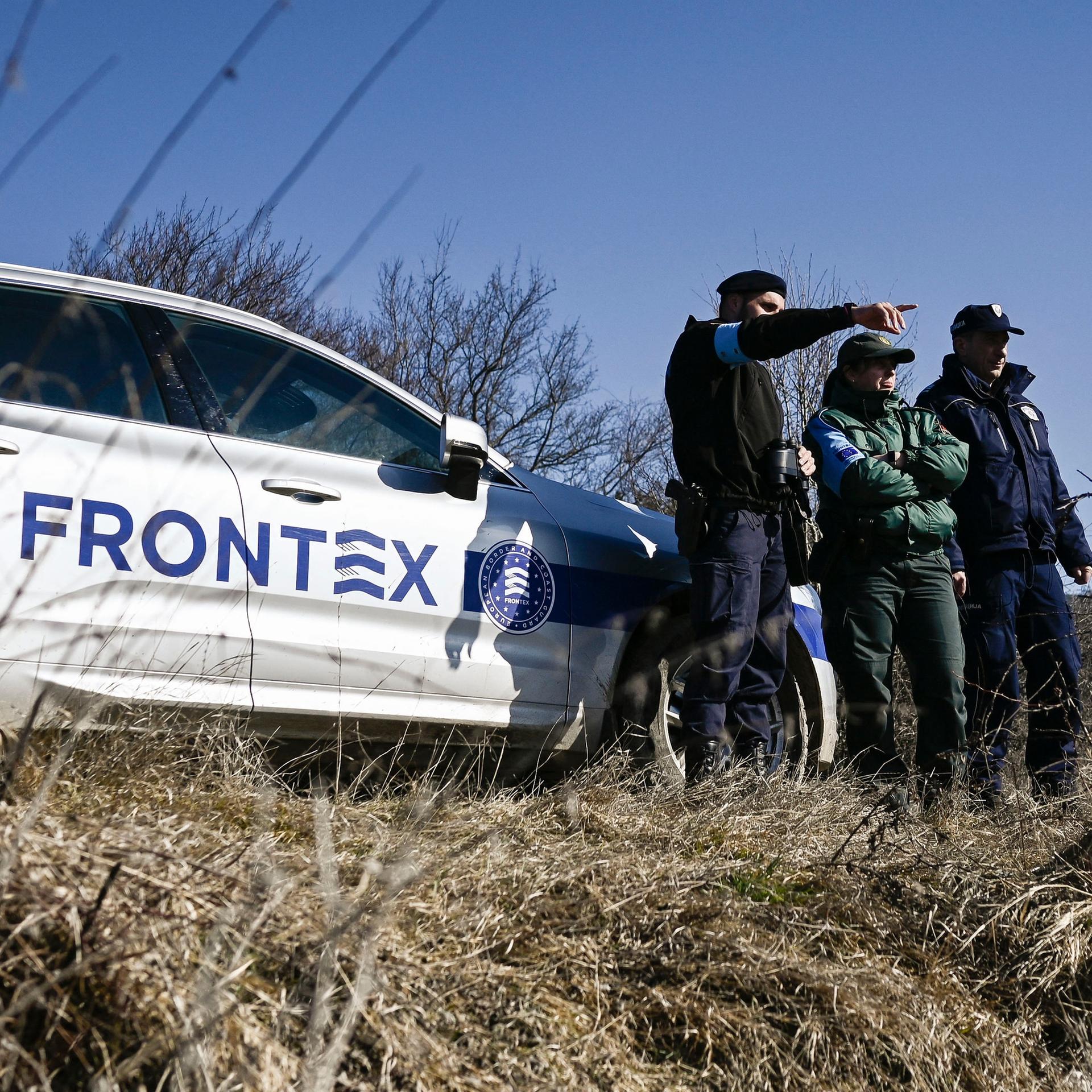 Drei uniformierte Männer stehen neben einem Wagen mit dem Frontex-Schriftzug und beobachten die Umgebung.