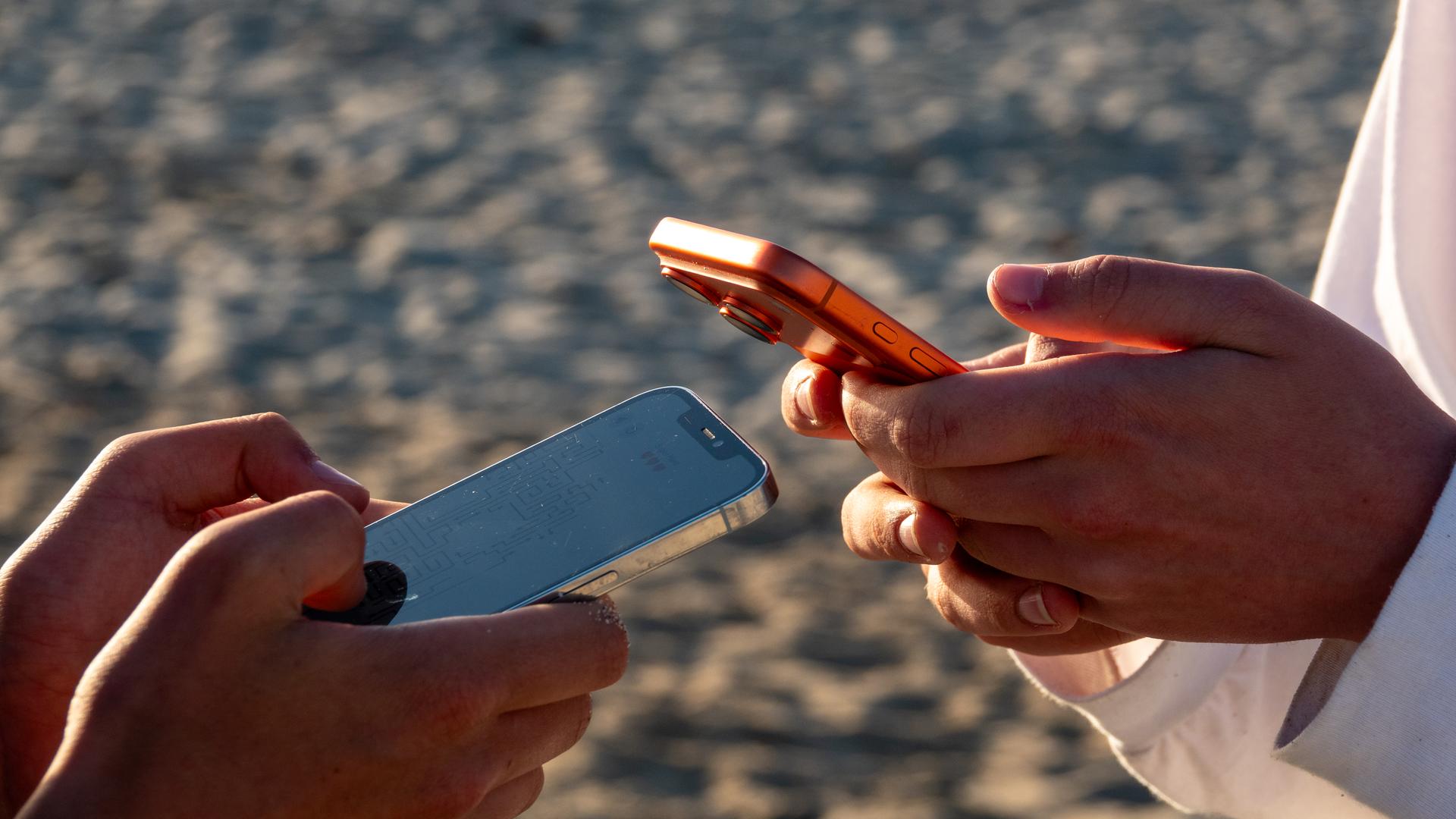 Die Hände von zwei Jugendlichen, die jeweils auf einem Mobiltelefon scrollen Die Hände von zwei Jugendlichen, die jeweils auf einem Mobiltelefon scrollen