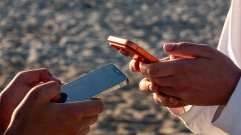 Die Hände von zwei Jugendlichen, die jeweils auf einem Mobiltelefon scrollen
