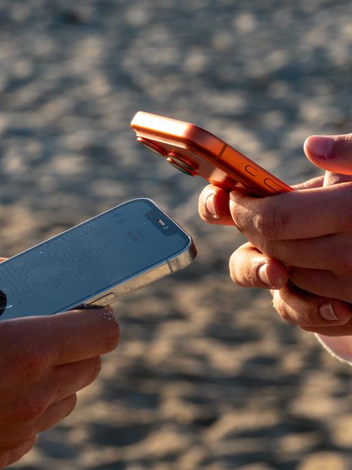 Die Hände von zwei Jugendlichen, die jeweils auf einem Mobiltelefon scrollen