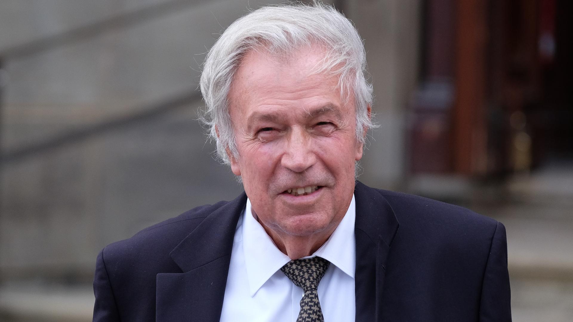 Das Bild zeigt einen fröhlich in die Kamera lächelnden Rainer Holbe mit Anzug, Krawatte und weißen Haaren.