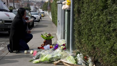 Eine Frau Kniet auf einem Gehweg, wo Blumen und Kerzen zum Gedenken stehen. 