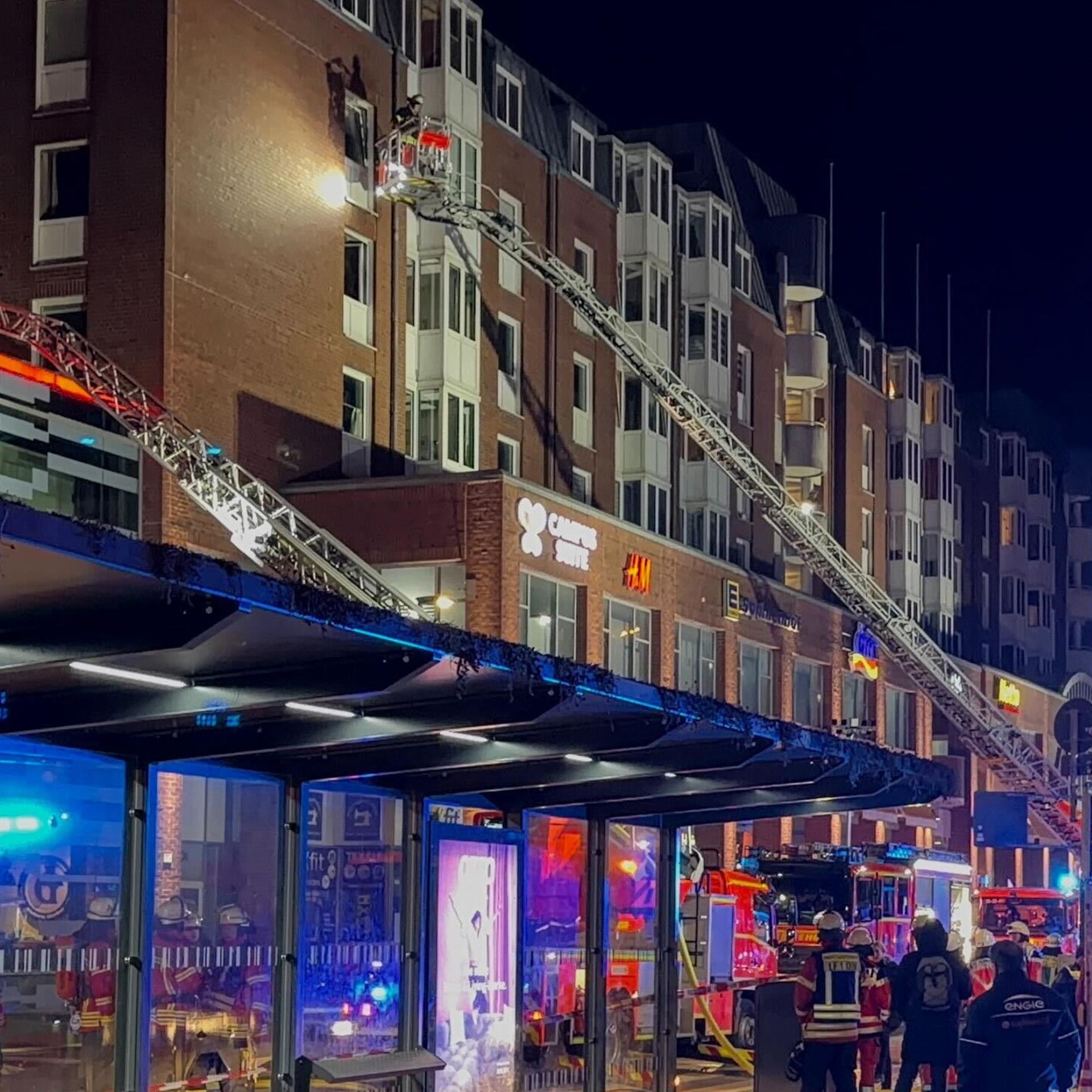 Einsatzkräfte der Feuerwehr arbeiten auf Drehleitern vor Balkonen eines Wohnhaus-Komplexes. 