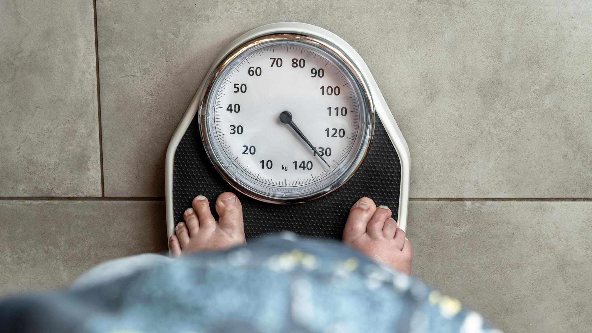 Eine erwachsene Frau steht barfuß auf einer Personenwaage, der Zeiger liegt über 130 kg. Eine erwachsene Frau steht barfuß auf einer Personenwaage, der Zeiger liegt über 130 kg.
