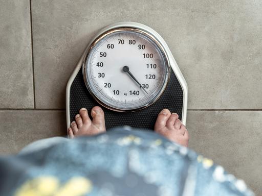 Eine erwachsene Frau steht barfuß auf einer Personenwaage, der Zeiger liegt über 130 kg. Eine erwachsene Frau steht barfuß auf einer Personenwaage, der Zeiger liegt über 130 kg.