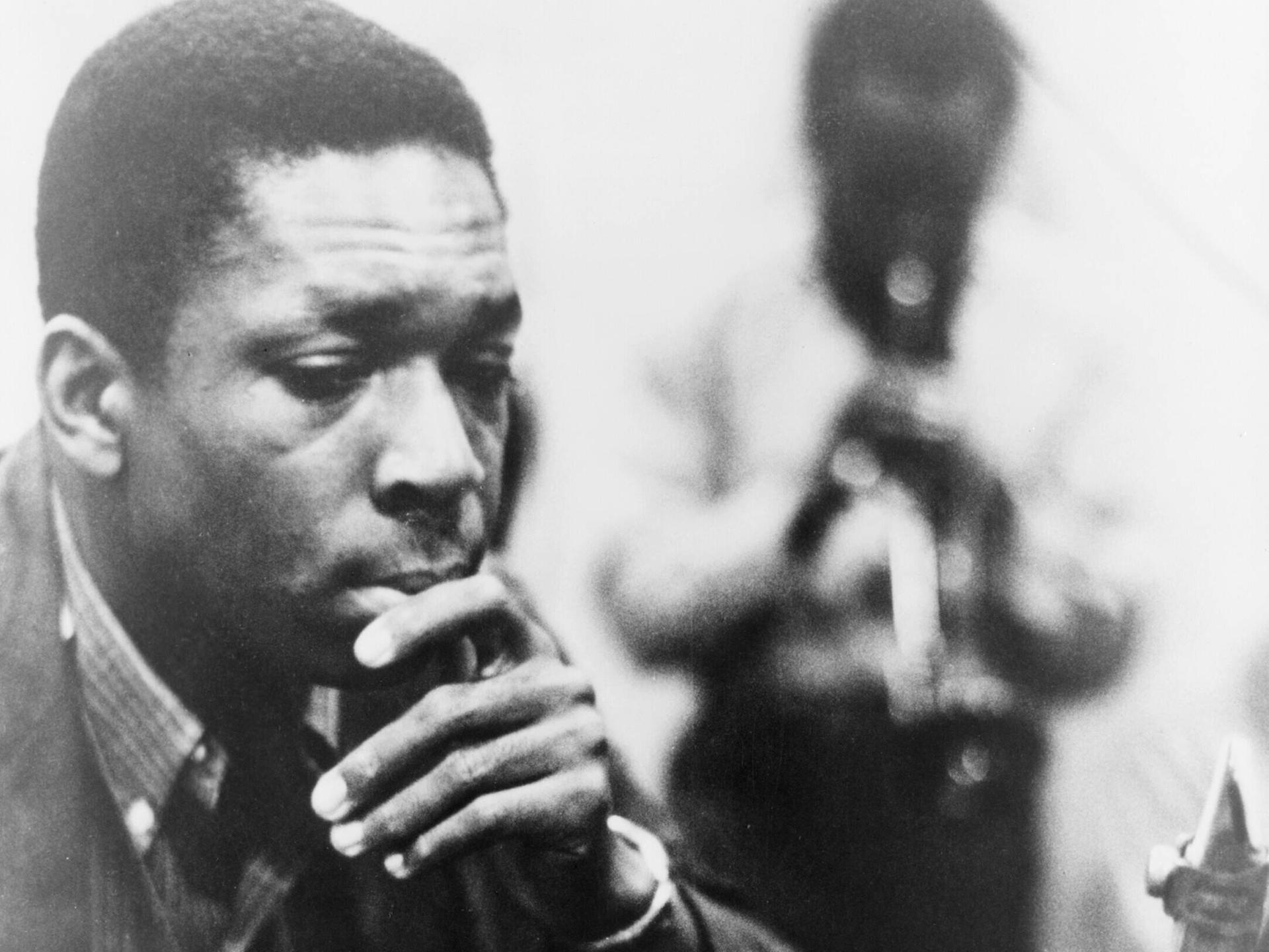 Schwarzweißaufnahme von John Coltrane, der sich nachdenklich die Hand ans Kinn hält Schwarzweißaufnahme von John Coltrane, der sich nachdenklich die Hand ans Kinn hält