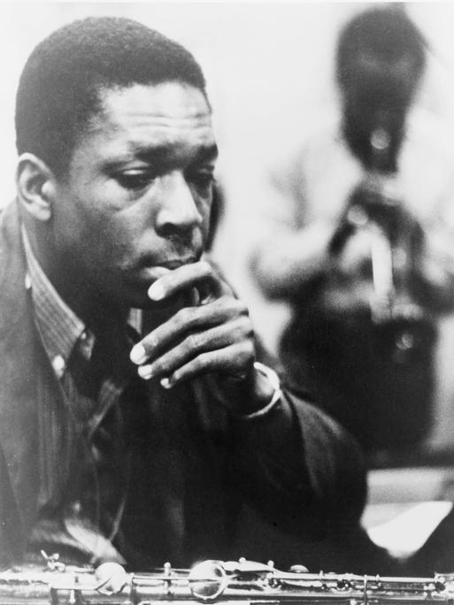 Schwarzweißaufnahme von John Coltrane, der sich nachdenklich die Hand ans Kinn hält