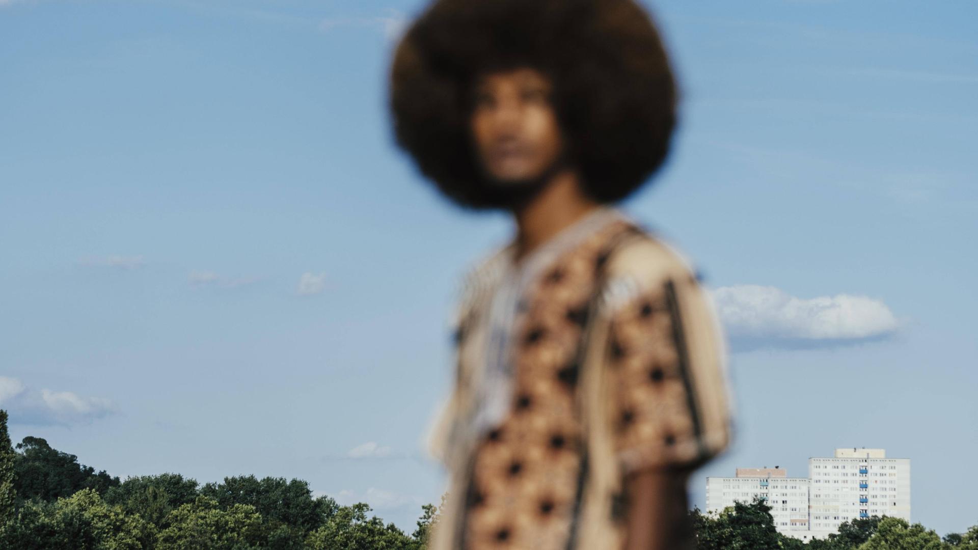 Unscharfes Bild eines Schwarzen Mannes mit Afrofrisur, der sich vor einem blauen Himmel abhebt.