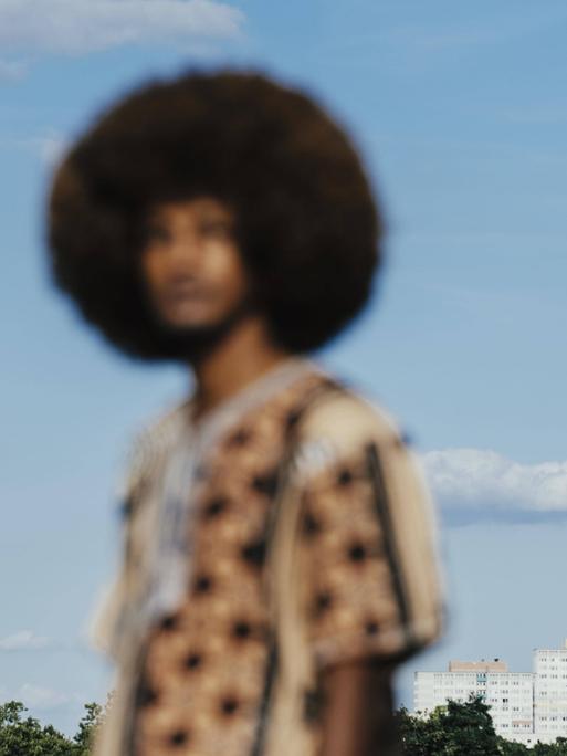 Unscharfes Bild eines Schwarzen Mannes mit Afrofrisur, der sich vor einem blauen Himmel abhebt.
