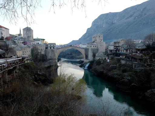 Eine Brücke führt über eine Fluss, der durch ein Tal fließt. Die Brücke verbindet Teile der Stadt Mostar.