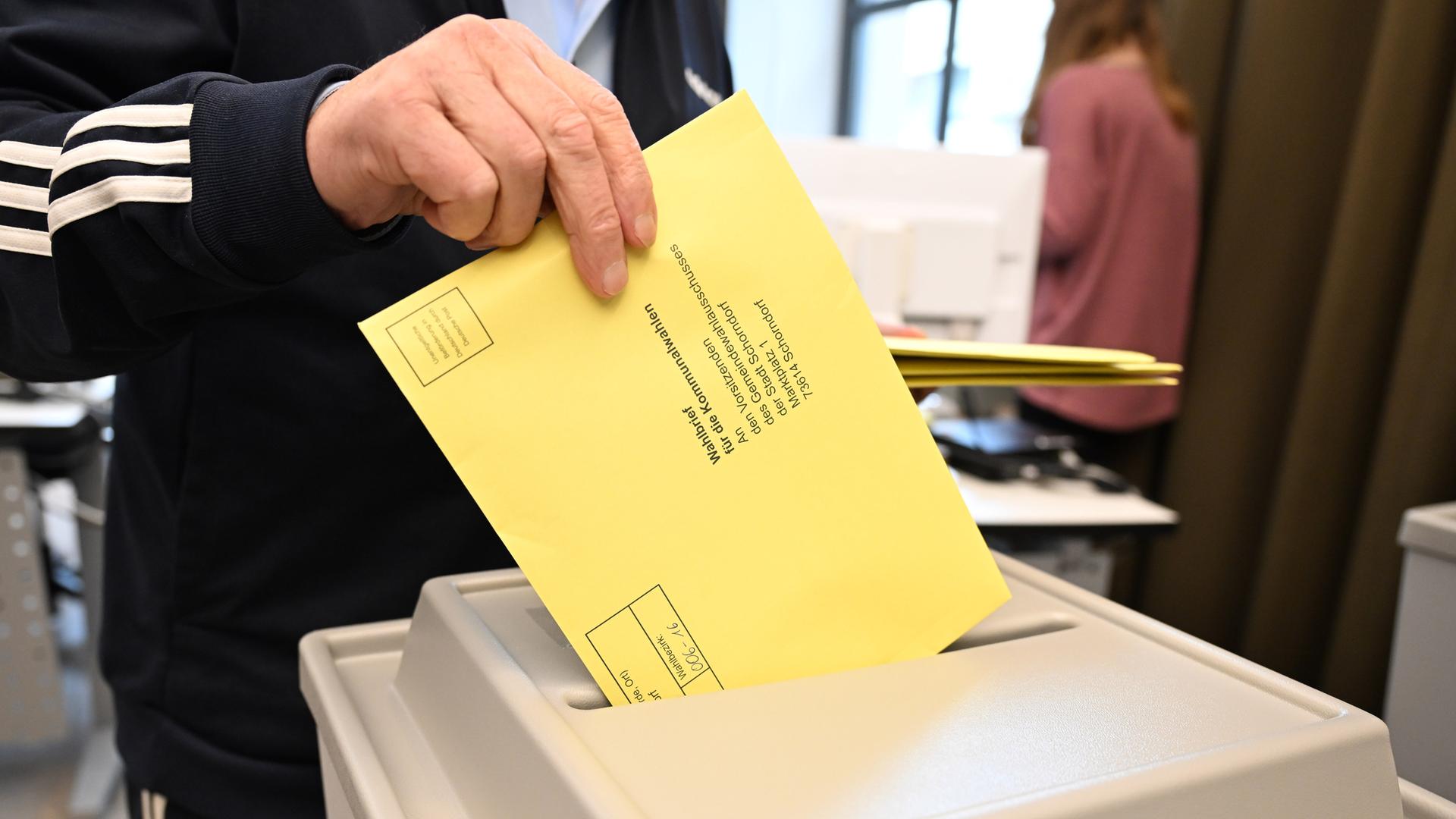 Ein Wahlbrief mit einem Stimmzettel für die Kommunalwahl wird im Rathaus in einem Wahllokal für die Briefwahl in eine Wahlurne gesteckt.