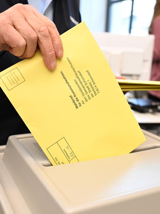 Ein Wahlbrief mit einem Stimmzettel für die Kommunalwahl wird im Rathaus in einem Wahllokal für die Briefwahl in eine Wahlurne gesteckt.