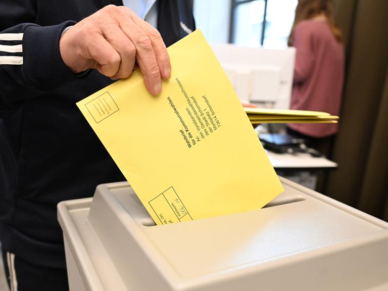 Ein Wahlbrief mit einem Stimmzettel für die Kommunalwahl wird im Rathaus in einem Wahllokal für die Briefwahl in eine Wahlurne gesteckt.