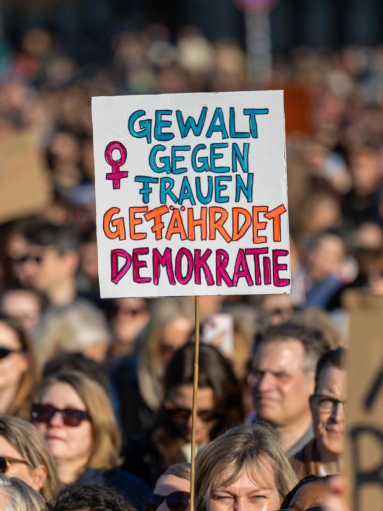 Zahlreiche Menschen protestieren auf der Straße gegen sexualisierte digitale Gewalt. Eine Person hält ein Schild hoch mit der Aufschrift "Gewalt gegen Frauen gefährdet Demokratie"