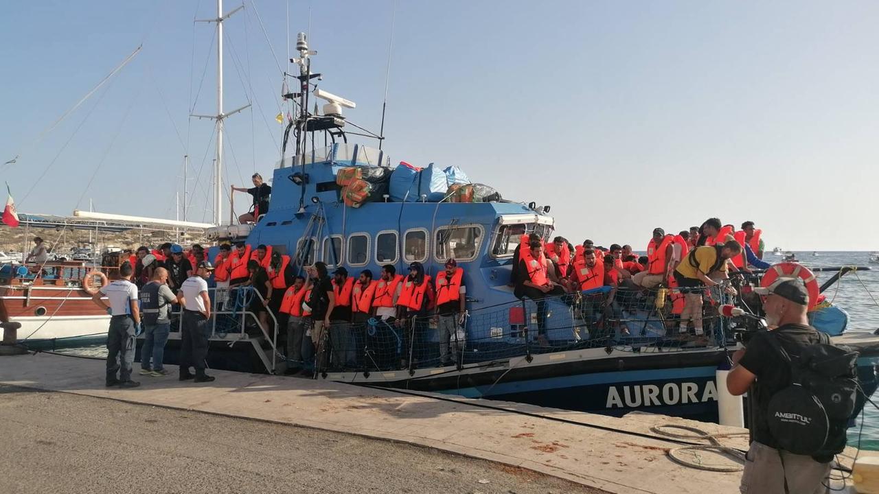 Zu sehen ist das deutsche Seenotrettungsschiff Aurora im Hafen von Lampedusa. An Bord befinden sich zahlreiche Menschen mit Rettungswesten.
