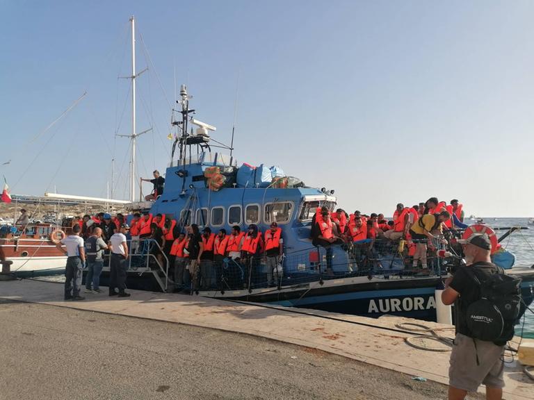 Zu sehen ist das deutsche Seenotrettungsschiff Aurora im Hafen von Lampedusa. An Bord befinden sich zahlreiche Menschen mit Rettungswesten.