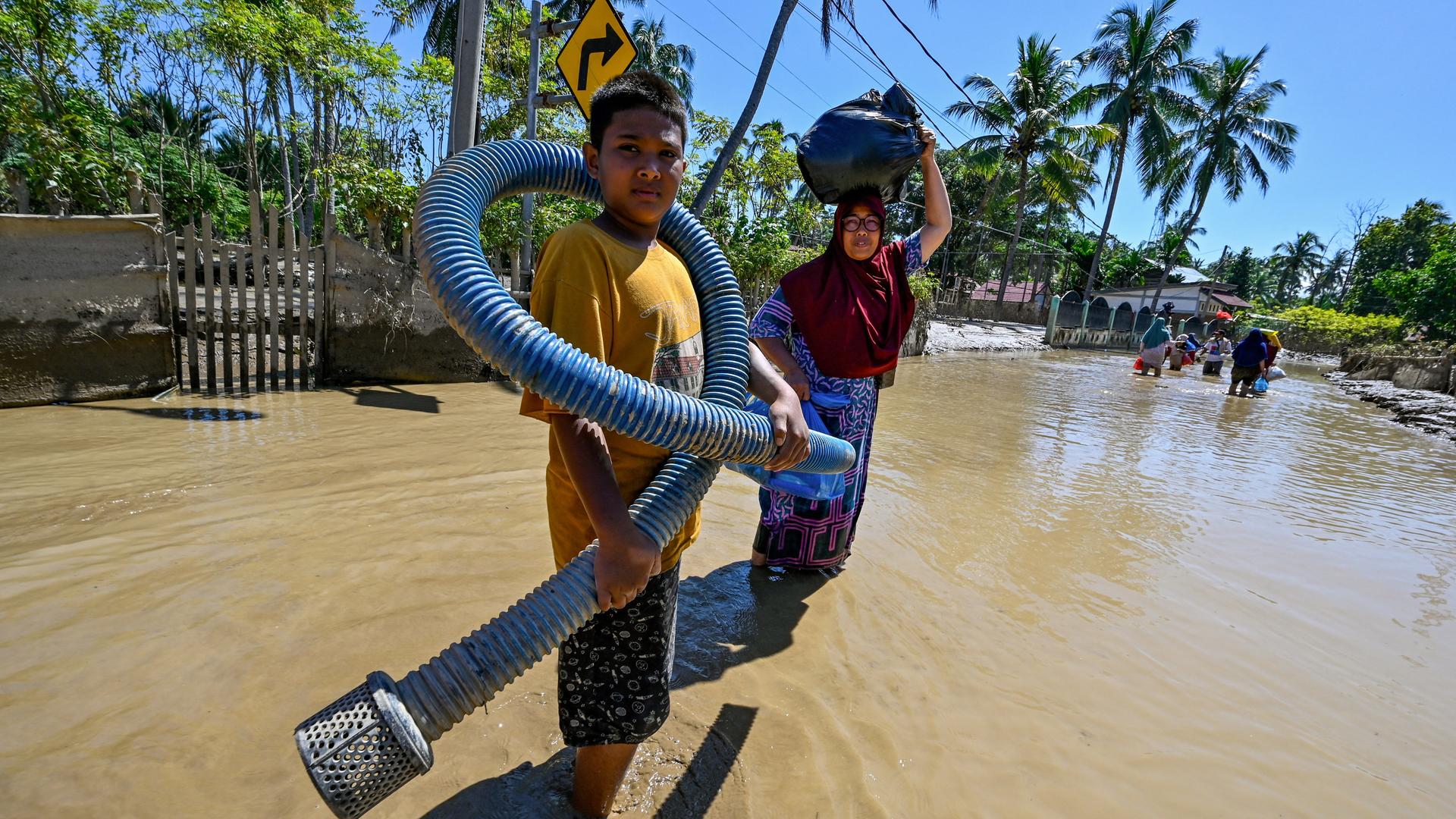 Ein Kind mit einem Metallschlauch und eine Frau auf einer überfluteten Straße in der indonesischen Provinz Aceh