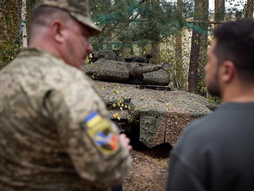 Bei einem Frontbesuch des urainischen Präsidenten ist im Hintergrund ein deutscher Leopard Panzer zu sehen.