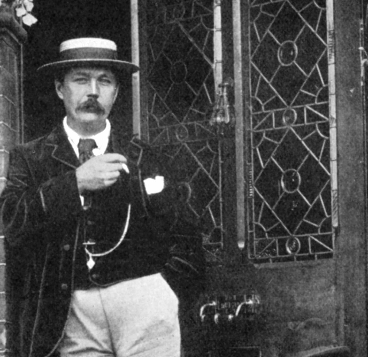 Der Schriftsteller Sir Arthur Conan Doyle (1859-1920) lehnt sich in einem Hauseingang an den Türrahmen und hat eine Pfeife in der Hand.