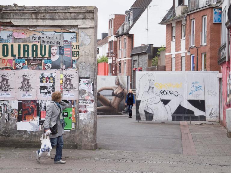 Man sieht den Eingang zur Rotlichtmeile Helenenstrasse in Bremen, im Hintergrund Graffitis von Frauen in Unterwäsche, im Vordergrund eine Frau mit Einkaufstüte