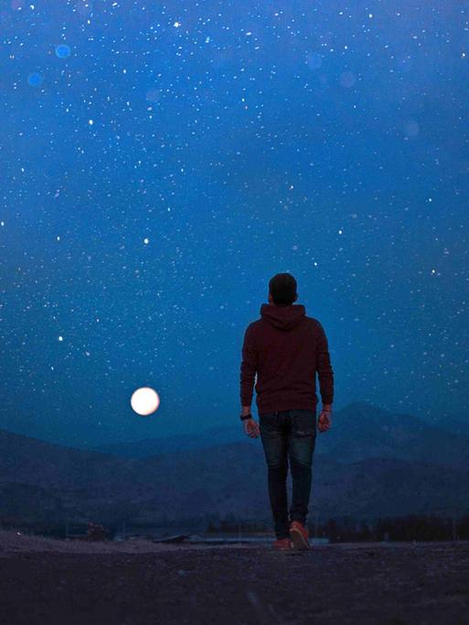 Ein Mann, mit dem Rücken zur Kamera, geht im Dunkeln in einer einsamen Landschaft dem Vollmond entgegen. Ein Mann, mit dem Rücken zur Kamera, geht im Dunkeln in einer einsamen Landschaft dem Vollmond entgegen.
