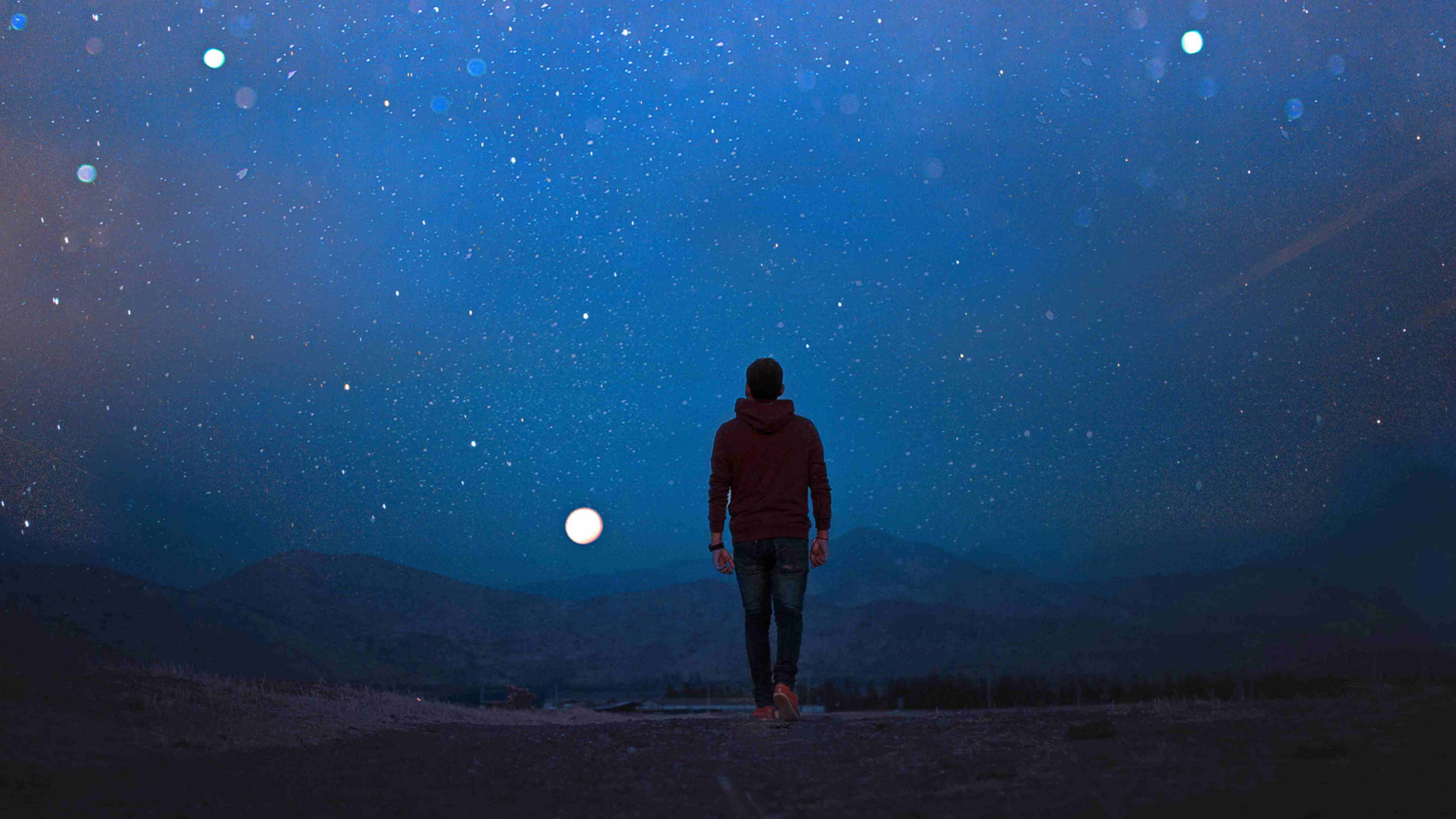 Ein Mann, mit dem Rücken zur Kamera, geht im Dunkeln in einer einsamen Landschaft dem Vollmond entgegen.