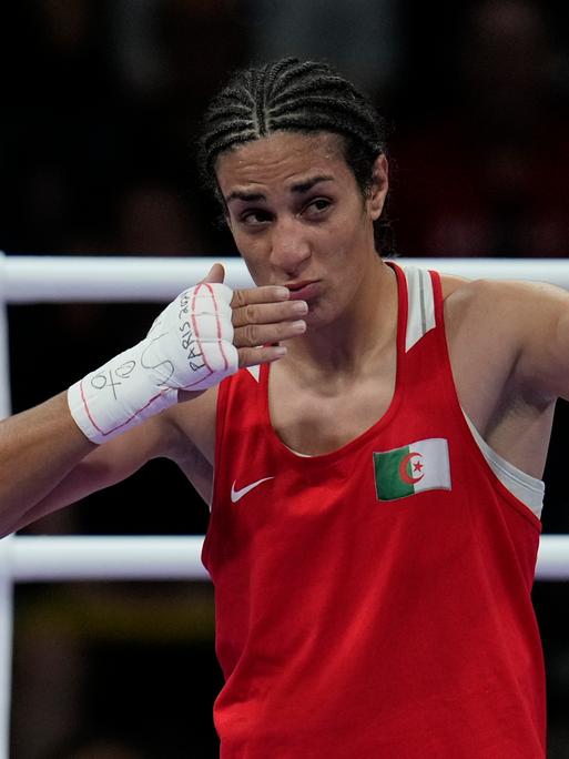 Die algerische Boxerin Imane Khelif. Sie trägt ein rotes Sporthemd und hält ihre weiß bandagierten Hände hoch.