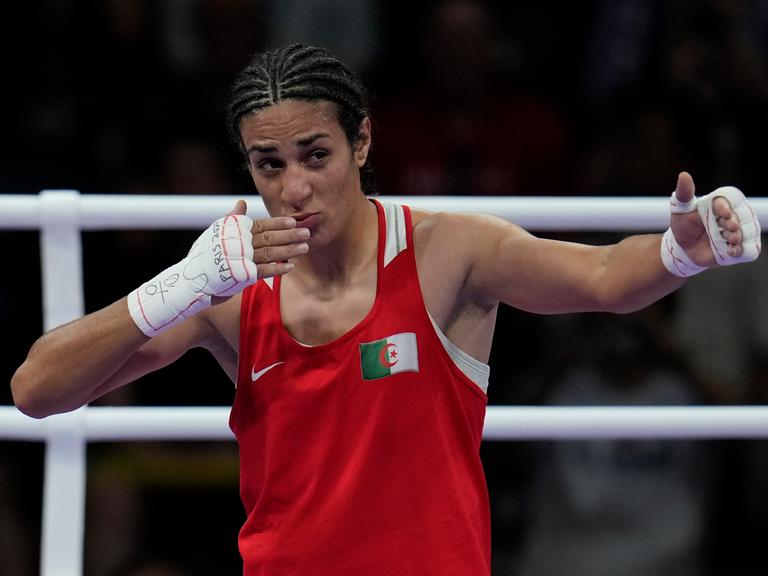 Die algerische Boxerin Imane Khelif. Sie trägt ein rotes Sporthemd und hält ihre weiß bandagierten Hände hoch.