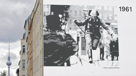 Auf einer Hauswand prangt ein Schwarz-Weiß-Foto, darauf zu sehen: Ein Polizist mit Geweht, der über einen Stacheldraht springt.