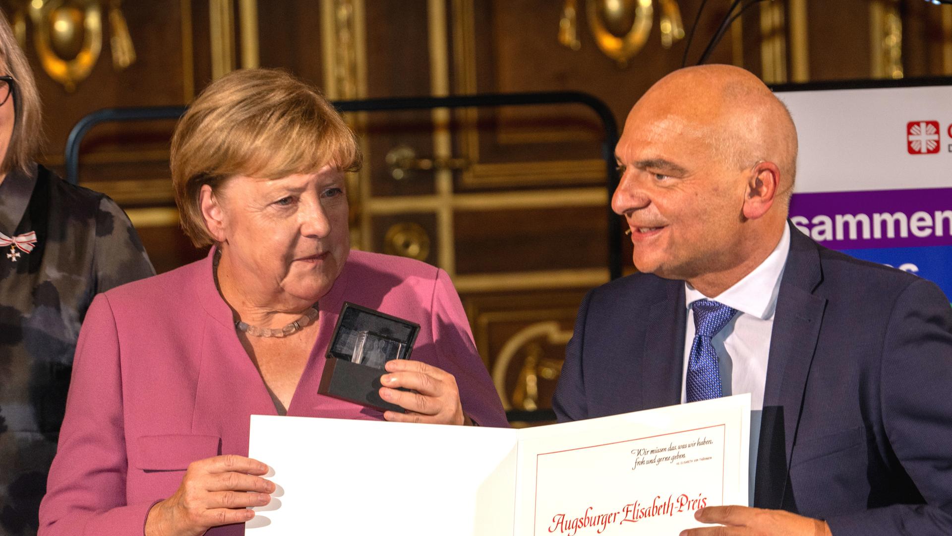 Die ehemalige Bundeskanzlerin Angela Merkel (CDU, l) erhält in Augsburg im Goldenen Saal des Rathauses von Caritasdirektor Markus Müller den Elisabeth-Preis. Foto: Stefan Puchner/dpa +++ dpa-Bildfunk +++
