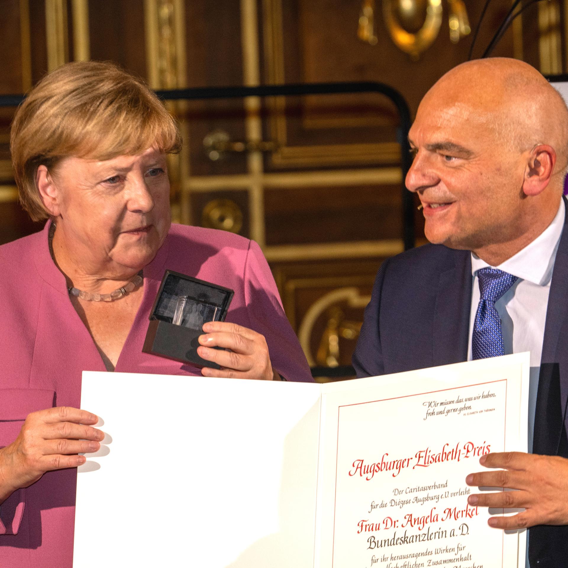 Die ehemalige Bundeskanzlerin Angela Merkel (CDU, l) erhält in Augsburg im Goldenen Saal des Rathauses von Caritasdirektor Markus Müller den Elisabeth-Preis. Foto: Stefan Puchner/dpa +++ dpa-Bildfunk +++