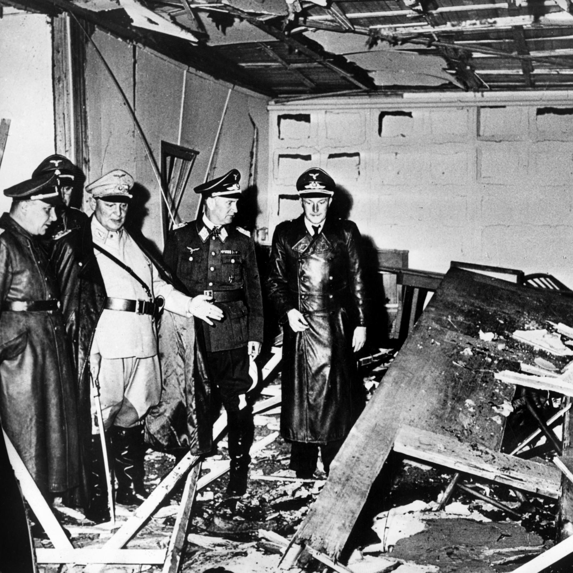 Schwarzweißfoto, das den zerstörten Raum nach dem Attentat zeigt: Reichsmarschall Hermann Göring (helle Uniform) und der Chef der "Kanzlei des Führers", Martin Bormann (l.), besichtigen den Raum der Karten-Baracke im Führerhauptquartier Rastenburg.