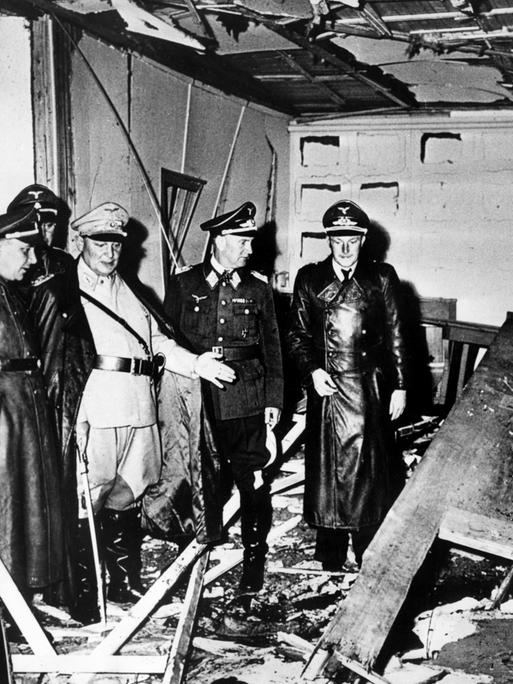 Schwarzweißfoto, das den zerstörten Raum nach dem Attentat zeigt: Reichsmarschall Hermann Göring (helle Uniform) und der Chef der "Kanzlei des Führers", Martin Bormann (l.), besichtigen den Raum der Karten-Baracke im Führerhauptquartier Rastenburg.