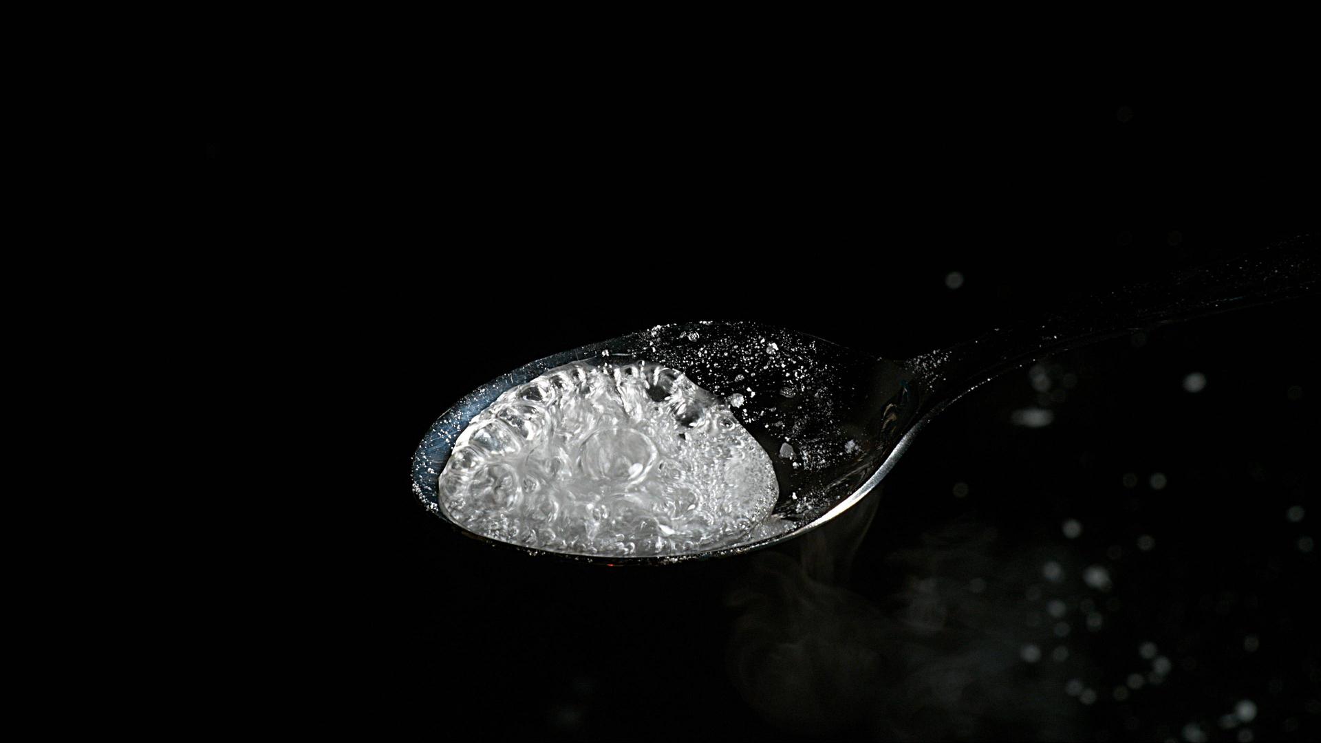 Weißes Kokainpulver in einem Löffel vor schwarzem Hintergrund