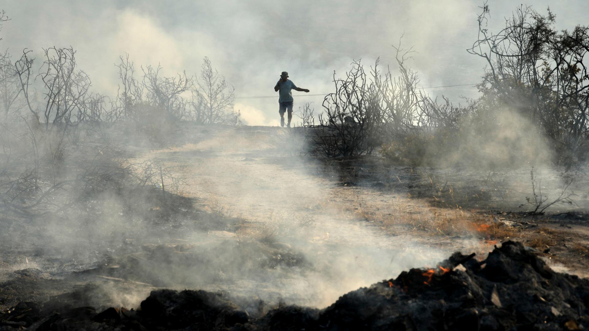 Ein Mann mit Handy, geht durch ein verbranntes Gebiet im Dorf Souni, während eines großen Waldbrandes auf der Südseite des Troodos-Gebirges im östlichen Mittelmeer.