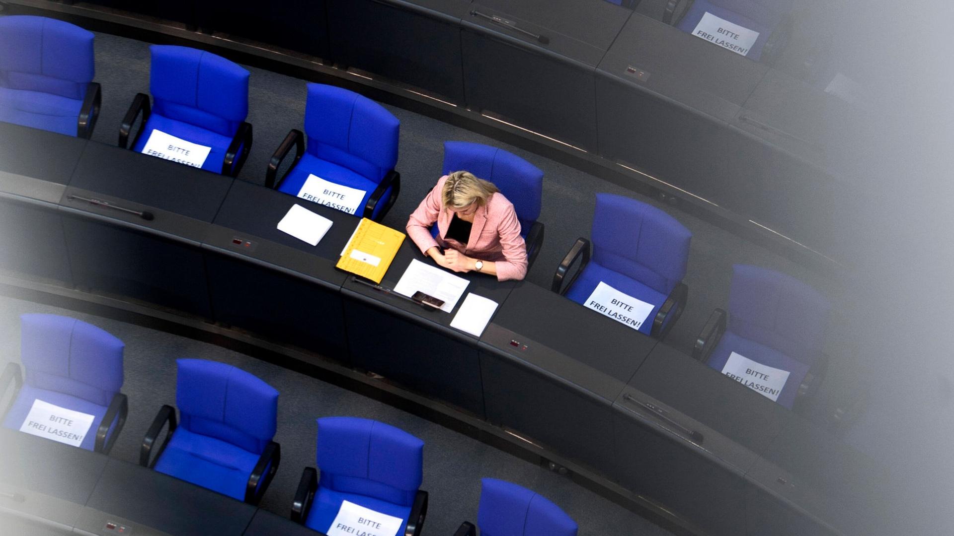 Vogelperspektive auf eine einzelne Abgeordnete, die im Plenarsaal des Bundestags sitzt.