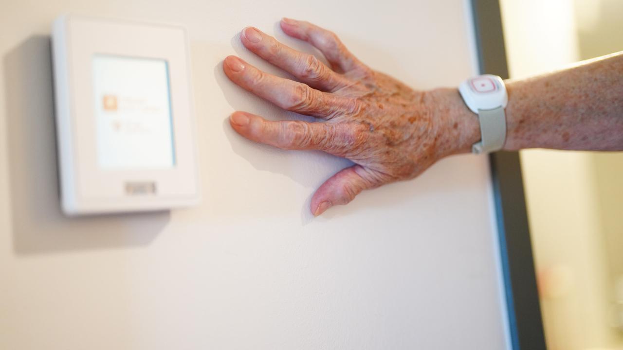 Die Hand einer Seniorin liegt an einer Wand. 