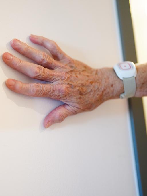 Die Hand einer Seniorin liegt an einer Wand. 