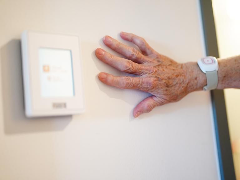 Die Hand einer Seniorin liegt an einer Wand. 