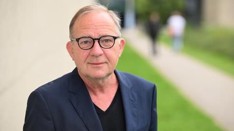 Der Schauspieler Uwe Preuss trägt eine schwarz umrandete Brille und ein dunkles Sakko und steht vor einer hellen Wand. Der Schauspieler Uwe Preuss trägt eine schwarz umrandete Brille und ein dunkles Sakko und steht vor einer hellen Wand.