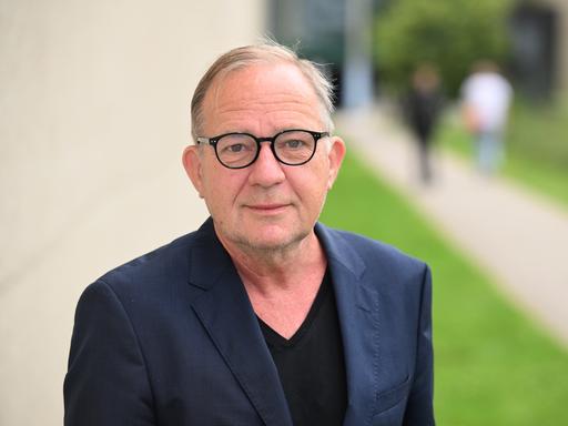 Der Schauspieler Uwe Preuss trägt eine schwarz umrandete Brille und ein dunkles Sakko und steht vor einer hellen Wand. Der Schauspieler Uwe Preuss trägt eine schwarz umrandete Brille und ein dunkles Sakko und steht vor einer hellen Wand.