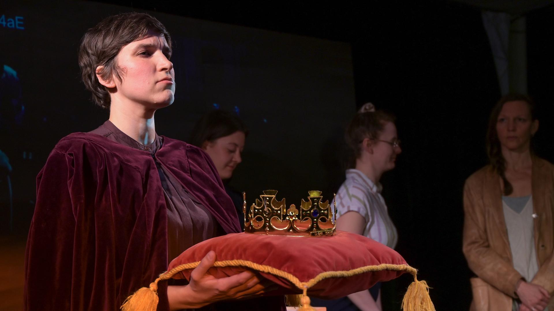 Die Schauspielerin Alessa Kordeck hält im Stück "König von Deutschland" die "Reichskrone", die auf einem Samtkissen liegt.  