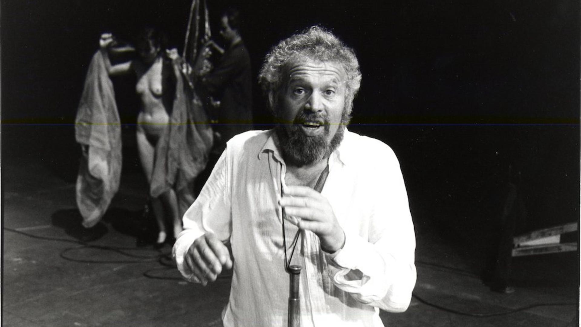 Otto M. Zykan auf der Bühne mit zwei Darstellern, darunter eine nackte Frau, im Hintergrund